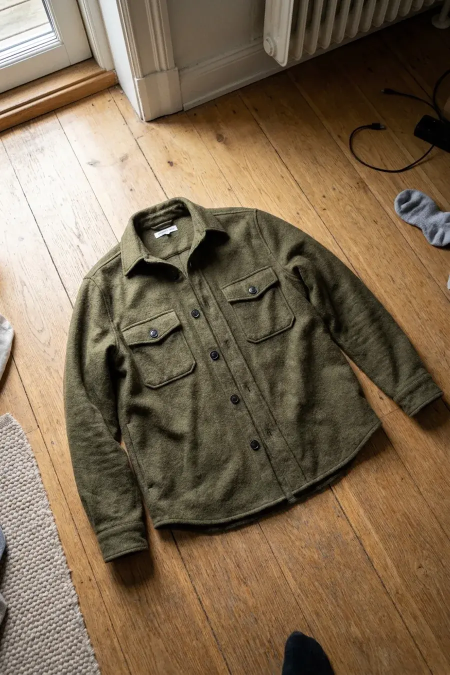 Olivengrøn ulds-overshirt lagt frem på trægulv