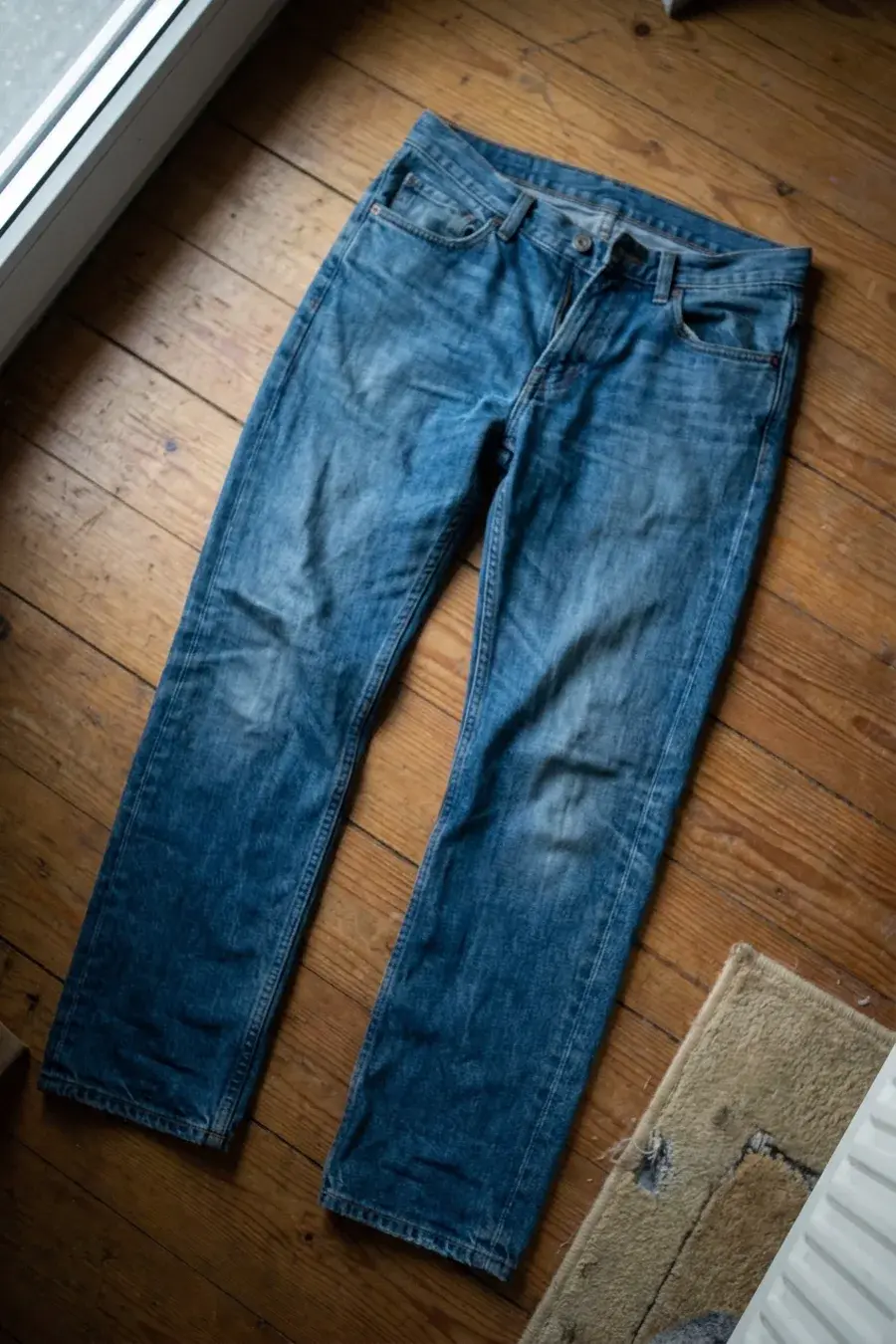 Mellemblå jeans lagt frem på trægulv